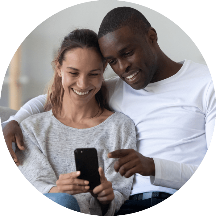 Title + Alt da imagem: Mulher e homem sorriem enquanto olham para o celular que está mãos da mulher. Imagem representa o plano TIM Live Internet Rural.
